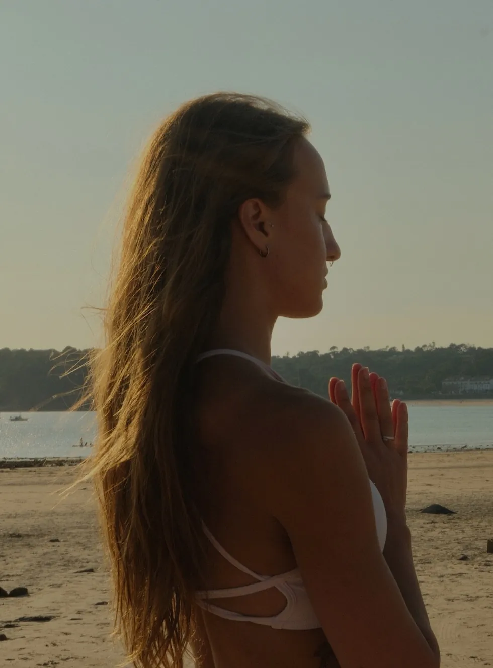 Naomi in profile with hands at prayer on the beach